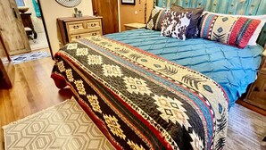 Un dormitorio con cama, cómoda de madera, espejo redondo, aire acondicionado instalado en la pared y alfombra estampada.