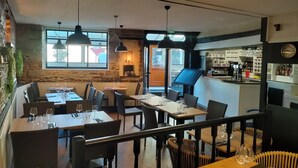 A restaurant with multiple tables and chairs, a bar area, and a stone wall. - Hotel Restaurant L'Esperance (Saint-Cast-le-Guildo)