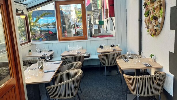 A restaurant with outdoor seating under a glass roof, tables with chairs, and a view of the street. - Hotel Restaurant L'Esperance (Saint-Cast-le-Guildo)
