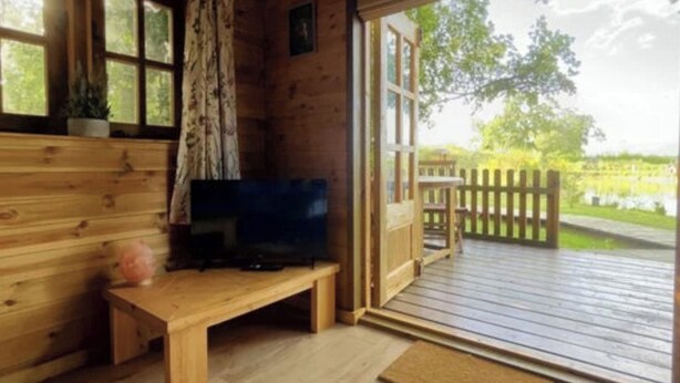 A wooden cabin with a TV on a bench, a door leading to an outdoor deck, and a view of a lake. - Inviting 1-bed Cabin in Newmarket (Newmarket)