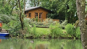 A wooden cabin surrounded by lush greenery and a calm pond with two boats. - Inviting 1-bed Cabin in Newmarket (Newmarket)