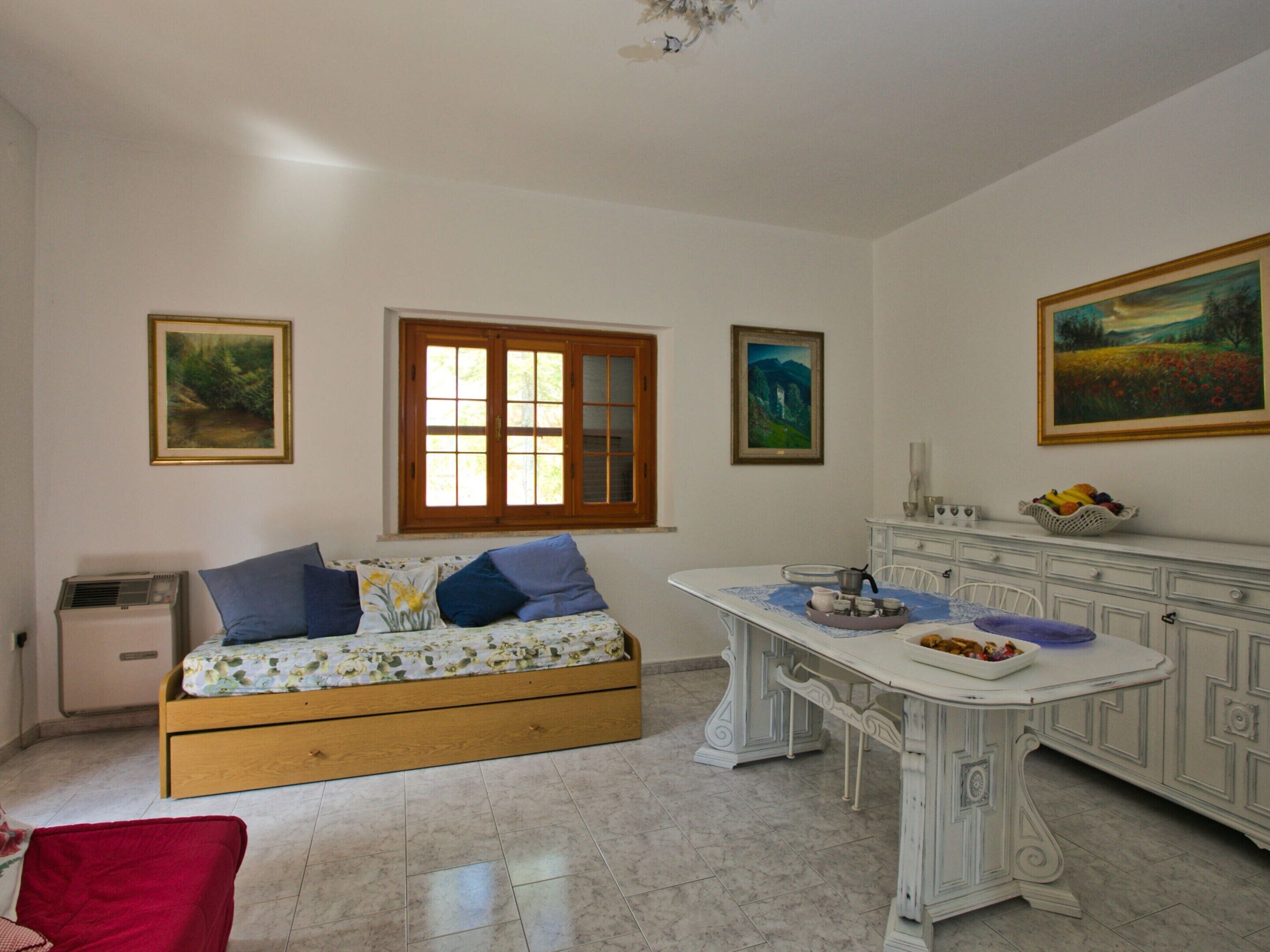 A room with a wooden sofa, a dining table with a white cabinet, and three paintings on the walls.