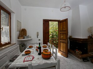 A dining area with a table set for four, a fireplace, and a view of a garden through an open door.