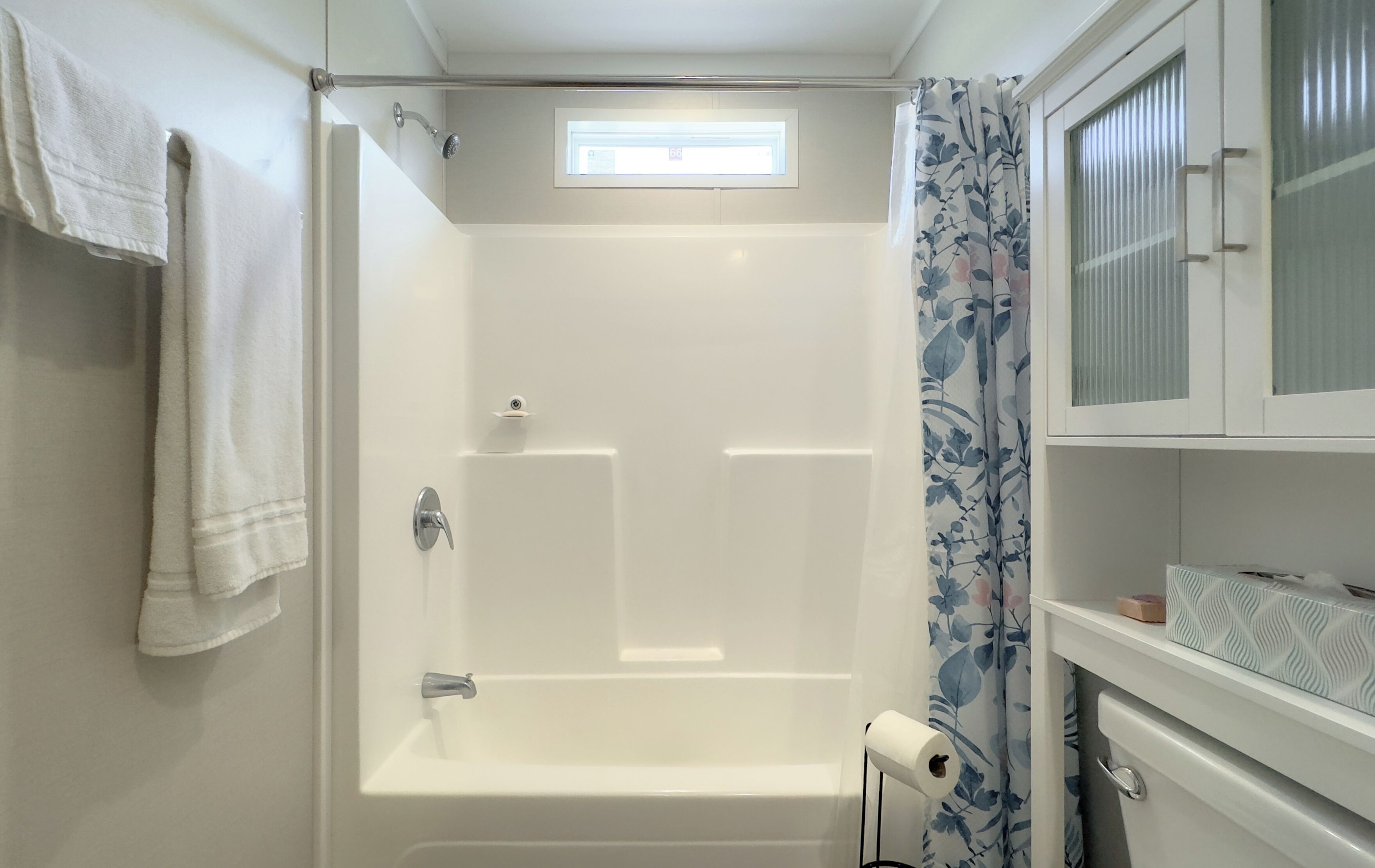 A bathroom with a shower, a toilet, and a window.