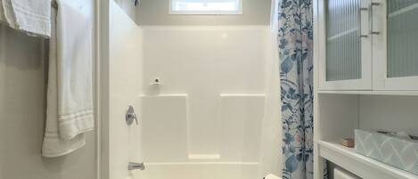 A bathroom with a shower, a toilet, and a window.