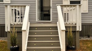 Un immeuble résidentiel doté d’un porche à l’avant, d’un escalier menant à une porte et de deux plantes en pot.