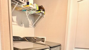 Une petite buanderie comprenant un lave-linge, un sèche-linge et une étagère au-dessus, où sont rangés divers objets.