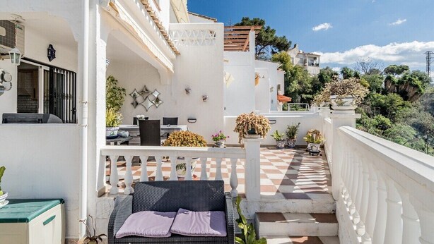 Un balcon agrémenté d’un canapé en osier, de plantes en pot et d’un sol à carreaux.