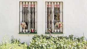 Deux fenêtres ornées de barreaux en métal noir et de rideaux roses, chacune agrémentée de compositions florales.