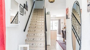 Un escalier orné de carreaux décoratifs, un mur blanc orné de photos encadrées et un luminaire suspendu.