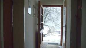 Een gang met een houten deur die uitkomt op een besneeid gebied buiten.