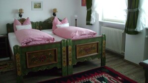 Een traditionele slaapkamer met een tweepersoonsbed, twee nachtkastjes, een rode hanglamp, een radiator en een raam met gordijnen.