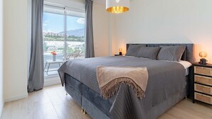 Un dormitorio con una cama grande, una mesita de noche, una lámpara y vistas a la ciudad a través de una ventana.