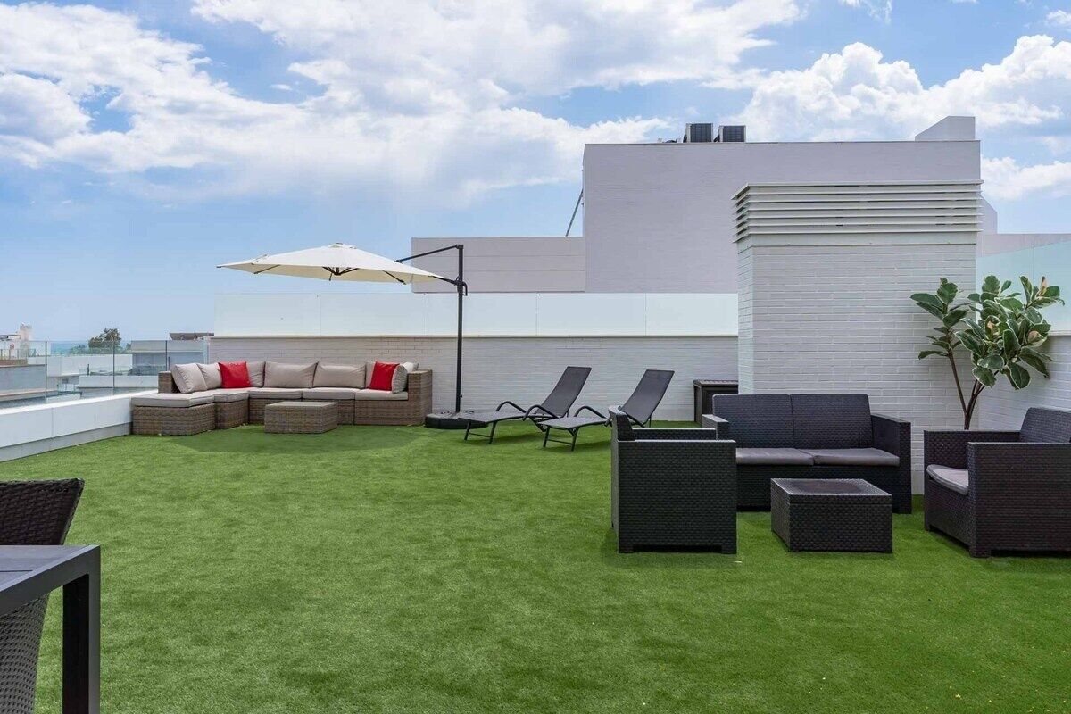A rooftop terrace with a green lawn, outdoor furniture, and a modern building in the background.
