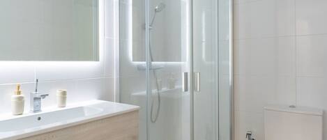 A modern bathroom with a glass-enclosed shower, a white sink with two bottles, and a toilet.