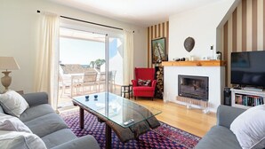 Uma sala de estar moderna com uma mesa de centro de vidro, sofás cinzas, uma poltrona vermelha, lareira e televisão.