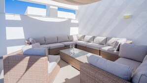 Een zonnig buitengebied met rieten meubels en een glazen bijzettafeltje.