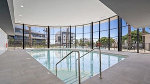 An indoor swimming pool with clear glass walls, a tiled floor, and a metal pool ladder. - Apartment with sea view and gym (Estepona)