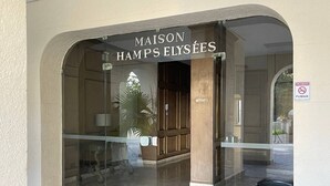 L'entrée de l'hôtel Maison Hamp's Elysées se compose d'une porte vitrée, d'un paillasson et d'une poubelle.