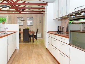 A modern kitchen with wooden flooring, white cabinetry, and a dining area with a table and chairs. - 4 Person Holiday Home in Glesborg (Glesborg)