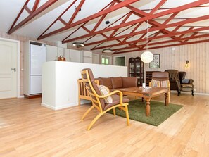 A spacious room with a high ceiling, wooden beams, a dining table with chairs, a sofa, and a cabinet. - 4 Person Holiday Home in Glesborg (Glesborg)