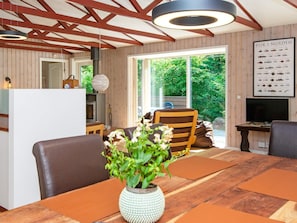 A modern interior with a wooden dining table, chairs, a vase with flowers, and a large window offering a view of greenery. - 4 Person Holiday Home in Glesborg (Glesborg)