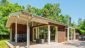 A wooden cabin with a covered patio, large sliding glass doors, and a deck. - 4 Person Holiday Home in Glesborg (Glesborg)