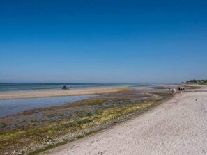 A beach with a clear sky, a sandy shore, and a few people walking.