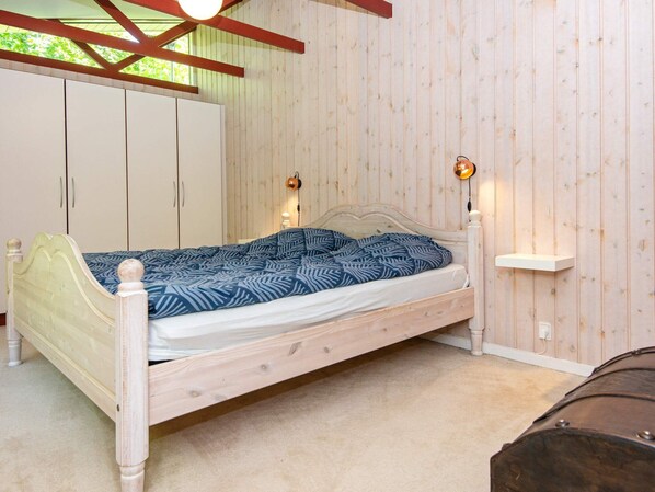 A single-bed room with a wooden headboard, a patterned bedspread, and a nightstand with a lamp.