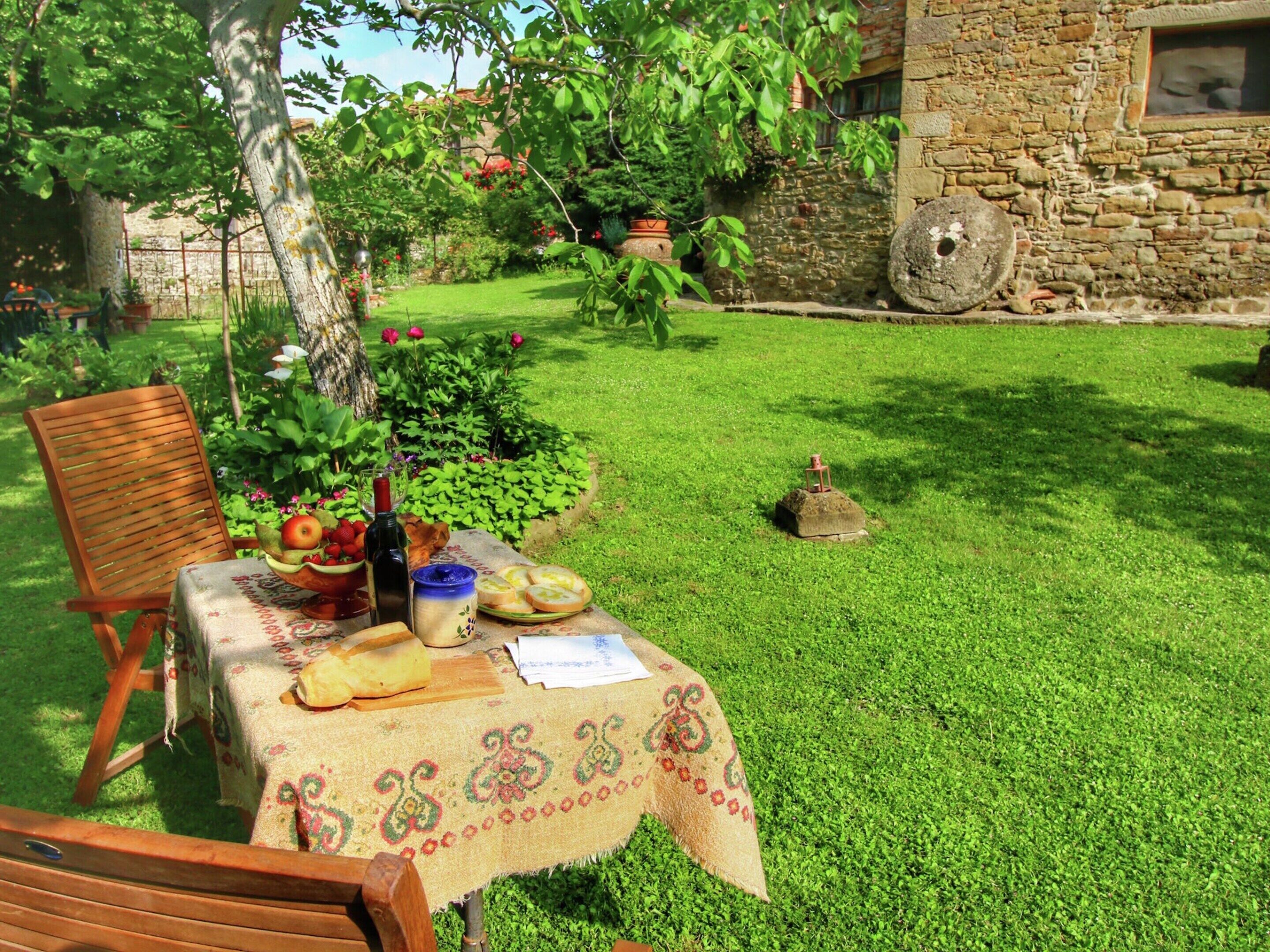 A table set outdoors with a tablecloth, a bottle, a bowl of fruit, and bread.