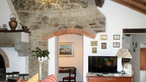 A cozy living room with a stone archway, a sofa, a television, and a wooden cabinet. - Farmhouse in Cortona With Pool (Cortona)