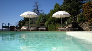 A clear swimming pool with lounge chairs and umbrellas. - Farmhouse in Cortona With Pool (Cortona)