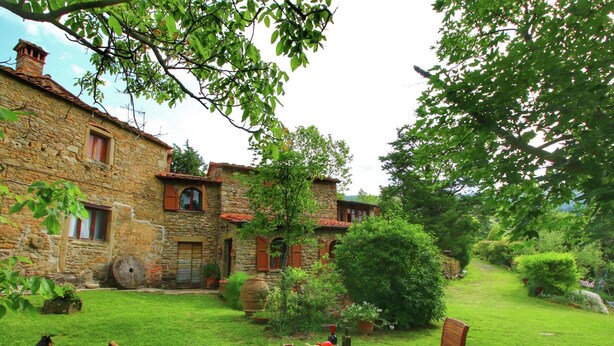 A stone building with a garden table set for dining, surrounded by lush greenery and a dog lying on the grass. - Farmhouse in Cortona With Pool (Cortona)