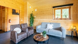 Een houten interieur met twee banken, een bijzettafeltje en een raam met uitzicht op groen.