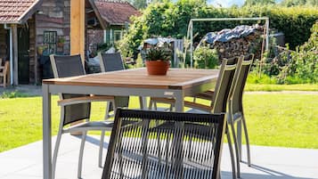 Een terras buiten met een houten tafel en stoelen, een plant in pot en een stenen muur op de achtergrond.