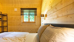 Een houten kamer met twee bedden, een raam met zonwering, een wandlamp en een hanglamp.