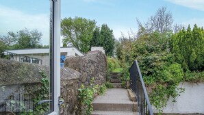 Un escalier menant à un bâtiment doté d’une porte en verre, entouré de verdure et de murs en pierre.