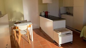 Een compacte keuken met een eethoek, een kleine koelkast, een koffiezetapparaat en een karretje met een dienblad.