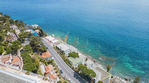 Vista aérea de uma cidade costeira com águas azul-claras, uma avenida principal e edifícios residenciais.