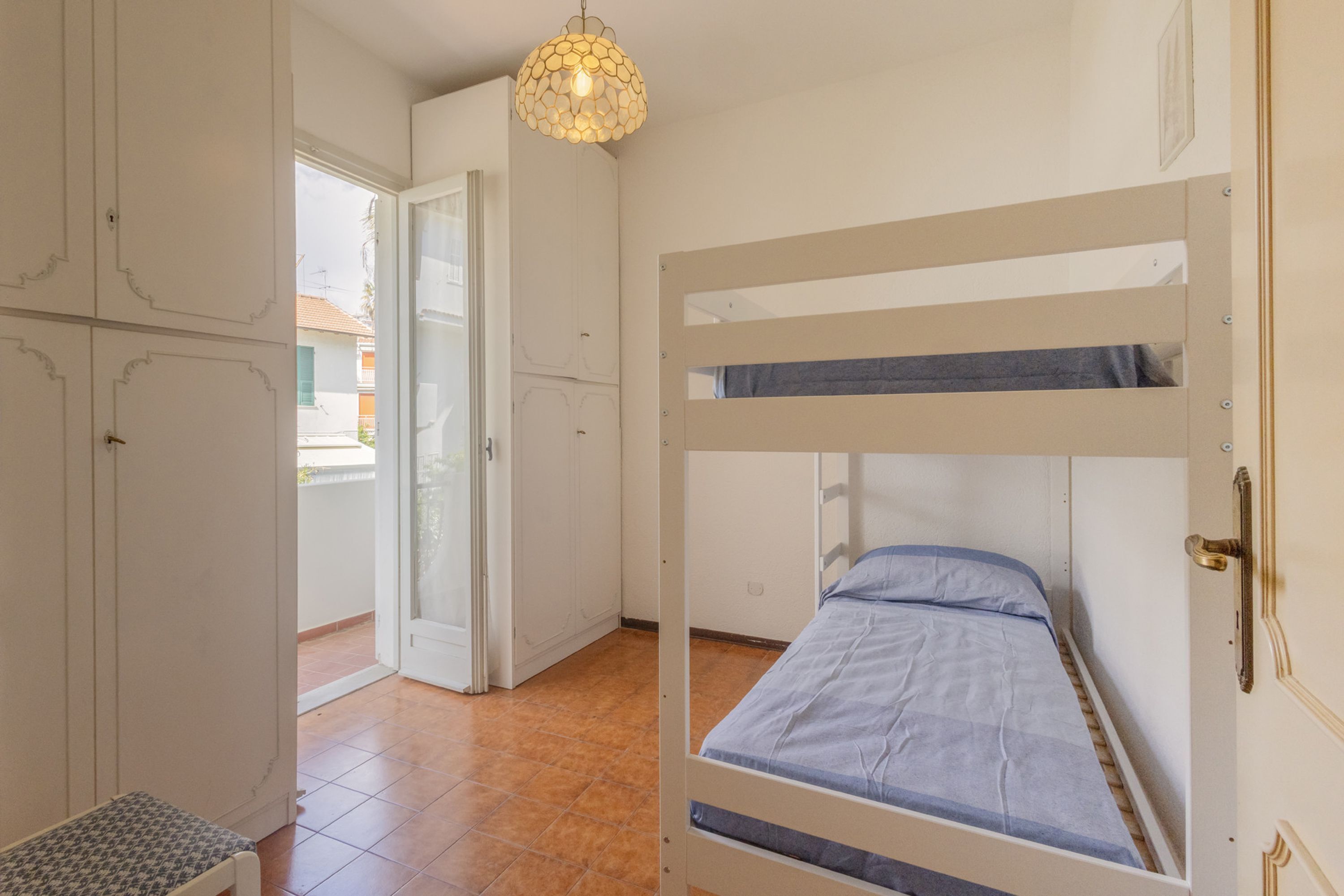 A room with a bunk bed, a bench, a wardrobe, and a door leading to a balcony.