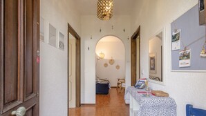 Un couloir avec une porte en bois, une table recouverte d’une nappe à motifs et un miroir accroché au mur.