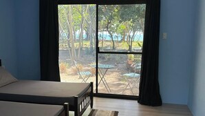 A bedroom with a bed, a ceiling fan, an air conditioning unit, and a view of a garden through a sliding door. - Magalong Beach Resort (Busuanga)