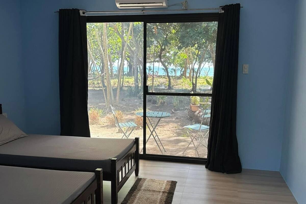 A bedroom with a bed, a ceiling fan, an air conditioning unit, and a view of a garden through a sliding door.