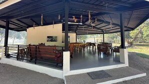 A covered outdoor seating area with wooden benches and tables, a concrete floor, and a view of the surrounding landscape. - Magalong Beach Resort (Busuanga)