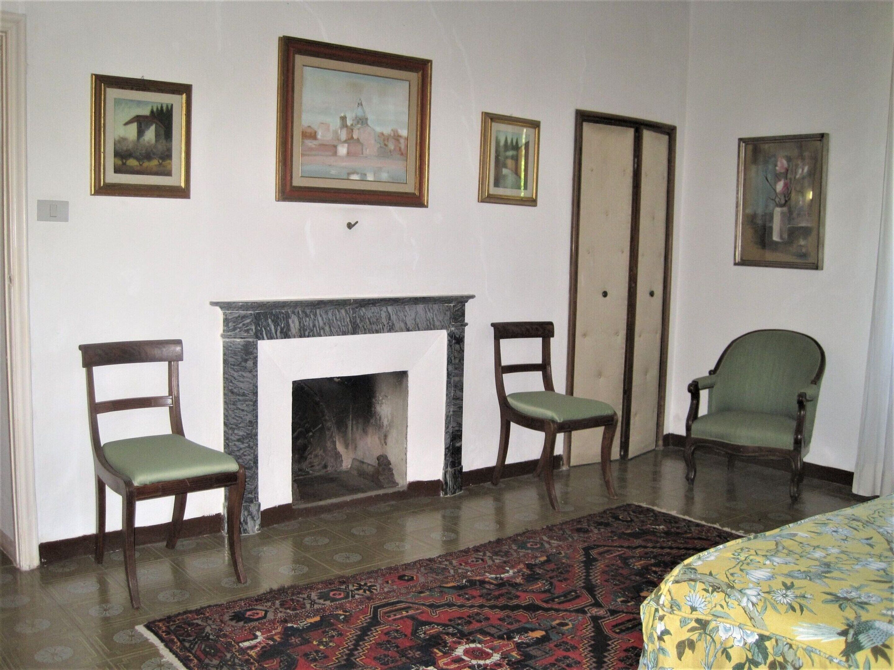 A room with a fireplace, three chairs, a patterned rug, and three framed pictures on the wall.