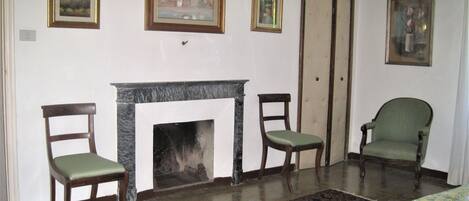 A room with a fireplace, three chairs, a patterned rug, and three framed pictures on the wall.