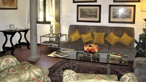 A living room with a sofa, armchairs, a coffee table, and a bookshelf. There are framed pictures on the wall and a window with curtains.