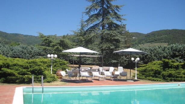 A swimming pool with lounge chairs and umbrellas, surrounded by greenery and hills.