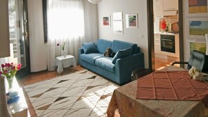 Un soggiorno con divano blu, tappeto decorato, tavolo da pranzo con tovaglia marrone e cucina sullo sfondo.