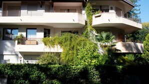 Un edificio residenziale a più piani con balconi, tetto in tegole e vegetazione circostante.